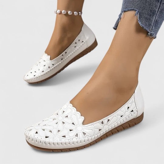 A woman wearing white floral cut-out slip-on flats on a warm, sunny day.