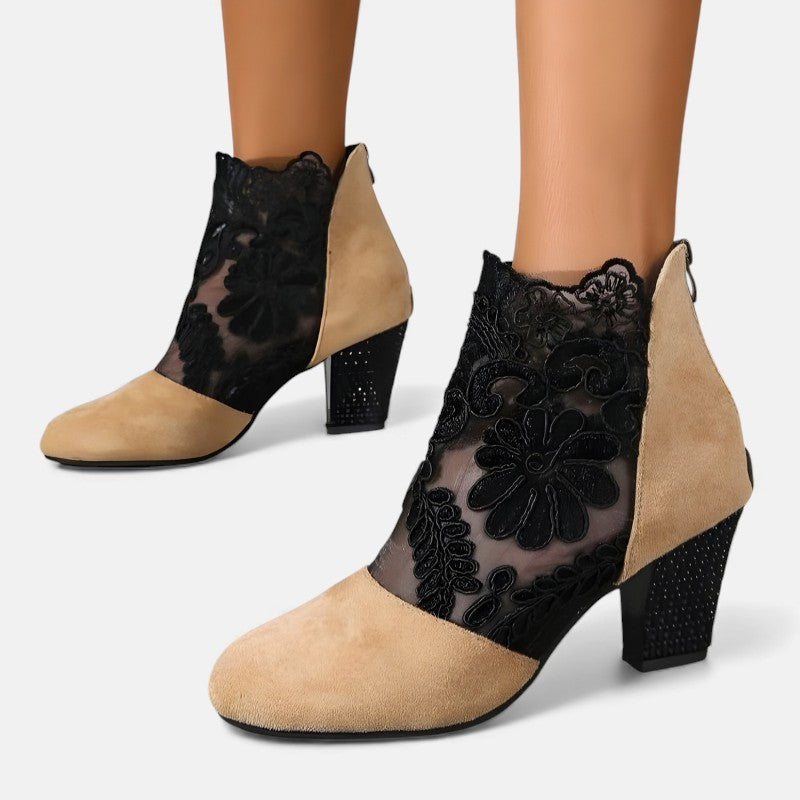 A woman wearing wine block-heel shoes with a sheer black floral-lace ankle overlay and a crystal-set heel