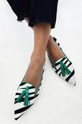 A woman wearing black-and-white zebra-stripe pointed flats finished with green tassels