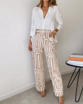 A woman wearing a plain button-up top with geometric-print pants and a belt at the waist.