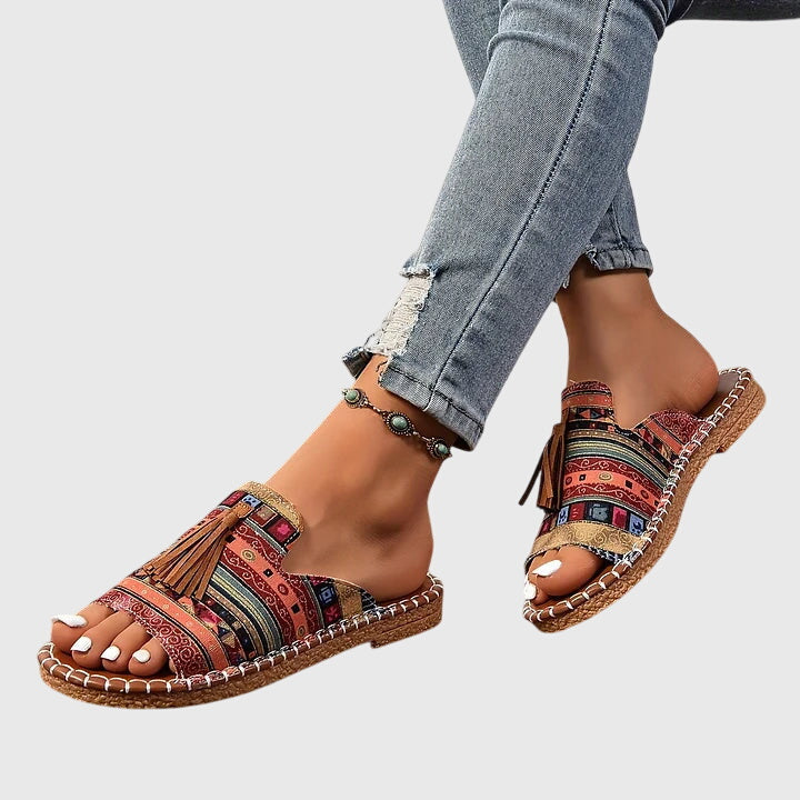 A woman wearing colourful patterned boho slides with tassel details on a holiday day out.