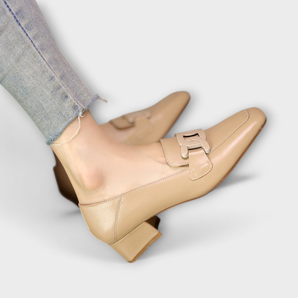 A pair of soft beige square-toe loafers with a chain-link ornament across the front.