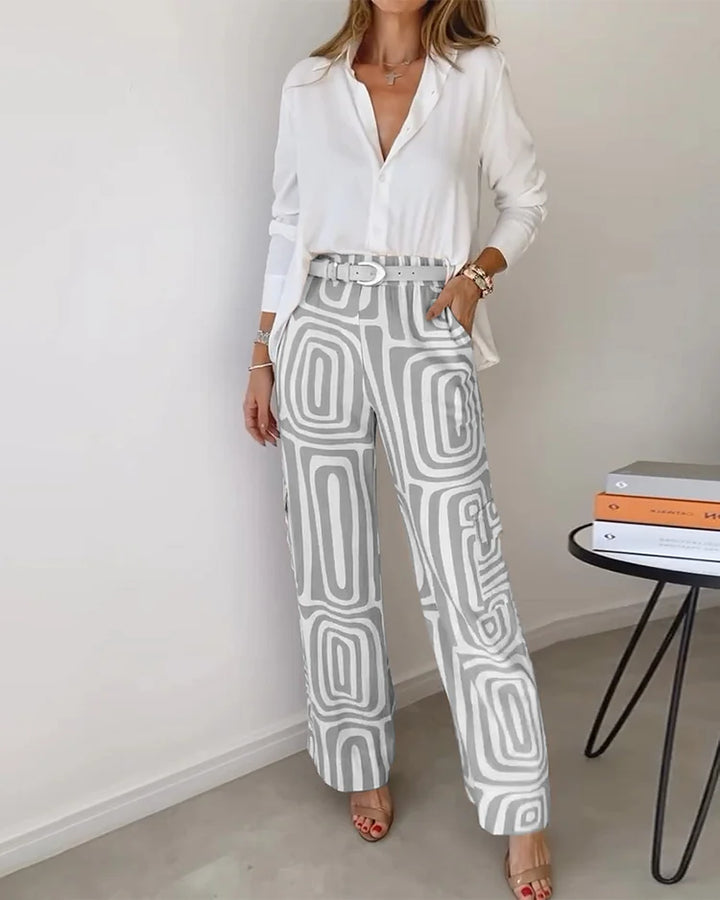 A woman wearing a plain button-up top with geometric-print pants and a belt at the waist.