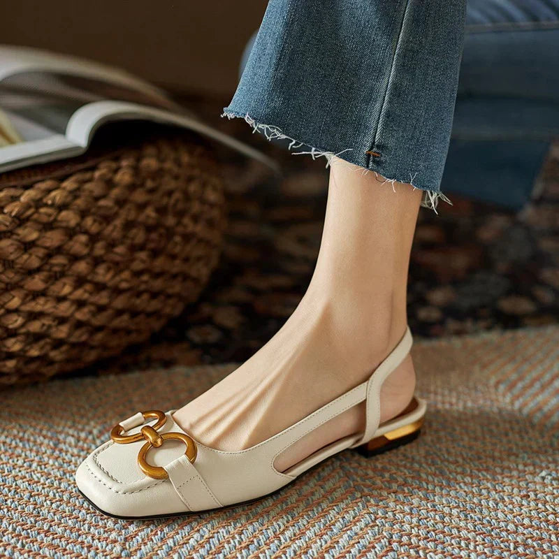 A woman wearing navy square-toe open-back flats with a small golden buckle detail.