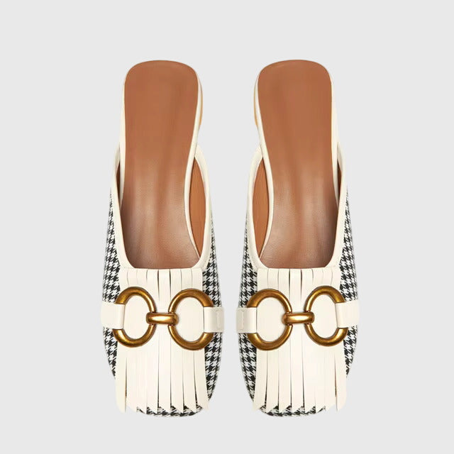 A cream closed-toe mule with a gold horsebit ring detail and a low heel.