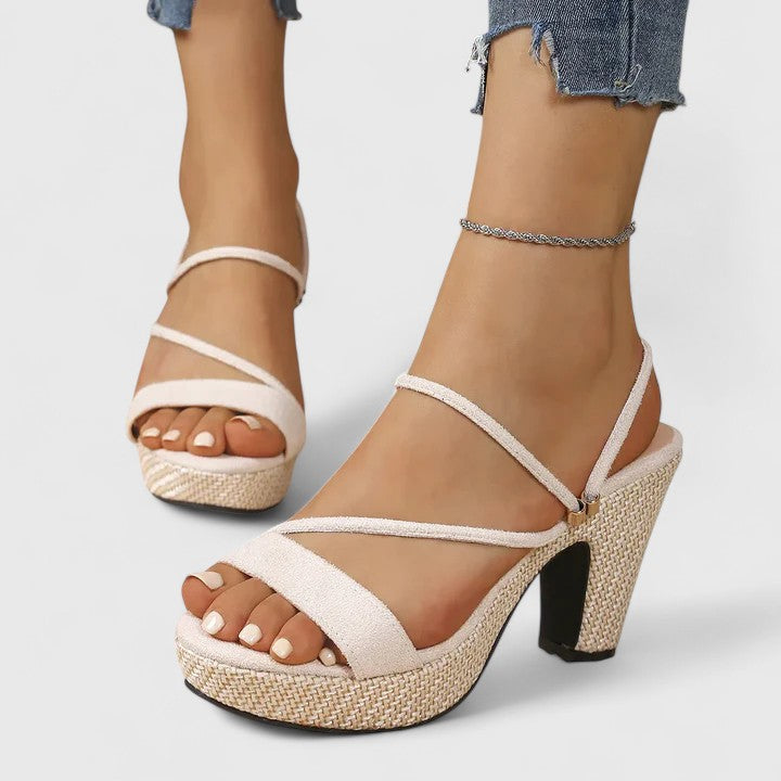 A woman in black strappy platform sandals with a chunky block heel, poised at an evening event.