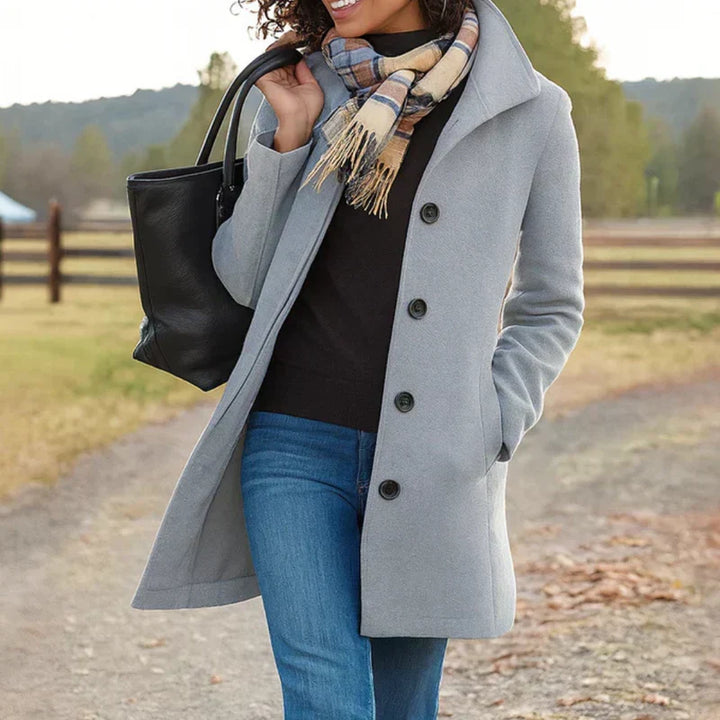 A woman wearing an elegant camel button-through coat over a sweater on a crisp fall day.