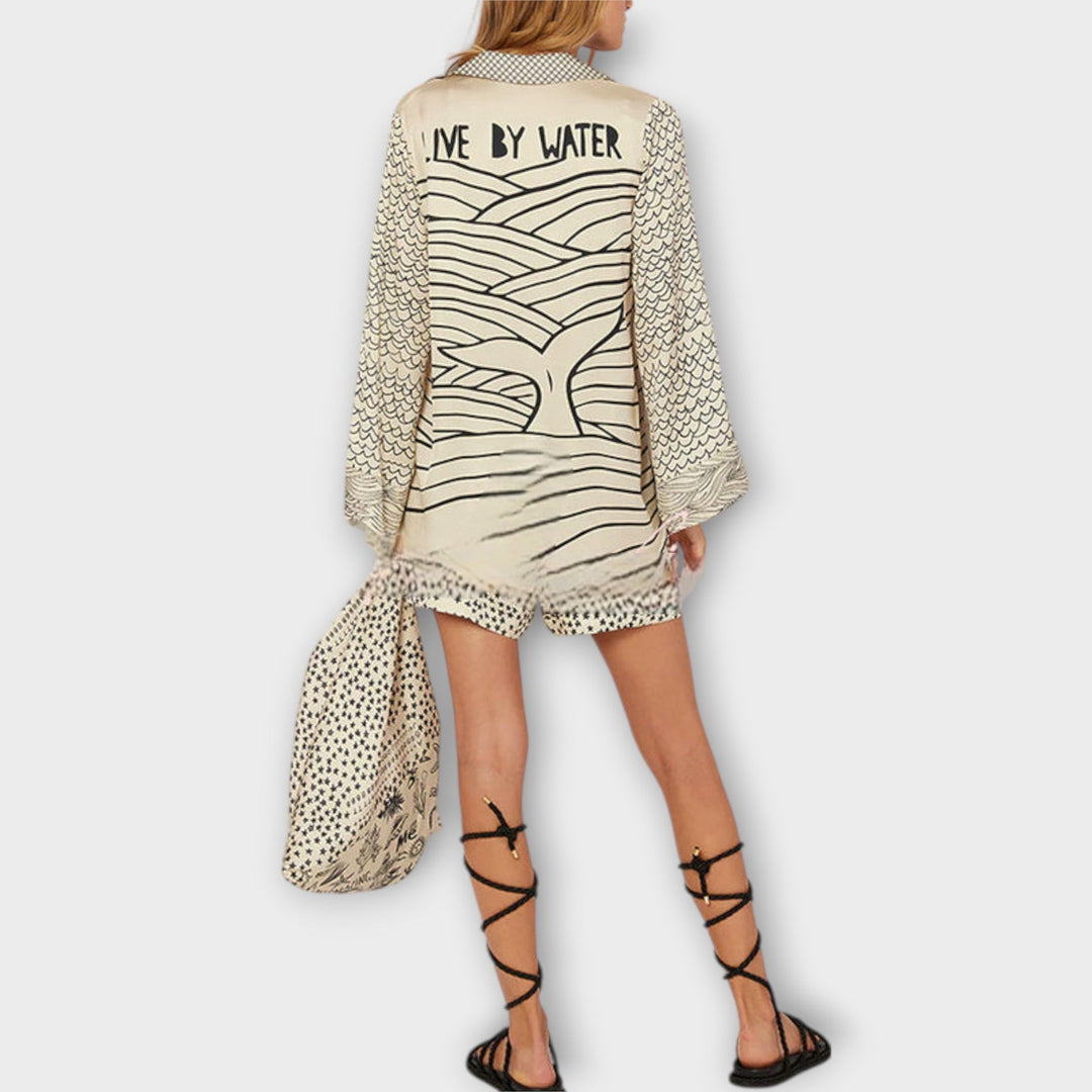 Woman walking on the beach in a relaxed tunic dress with playful maritime print and tie collar.
