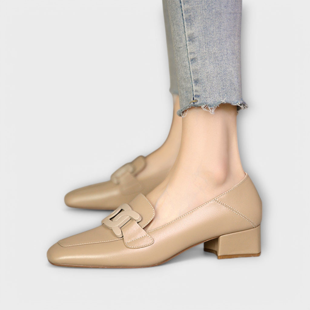 A pair of soft beige square-toe loafers with a chain-link ornament across the front.