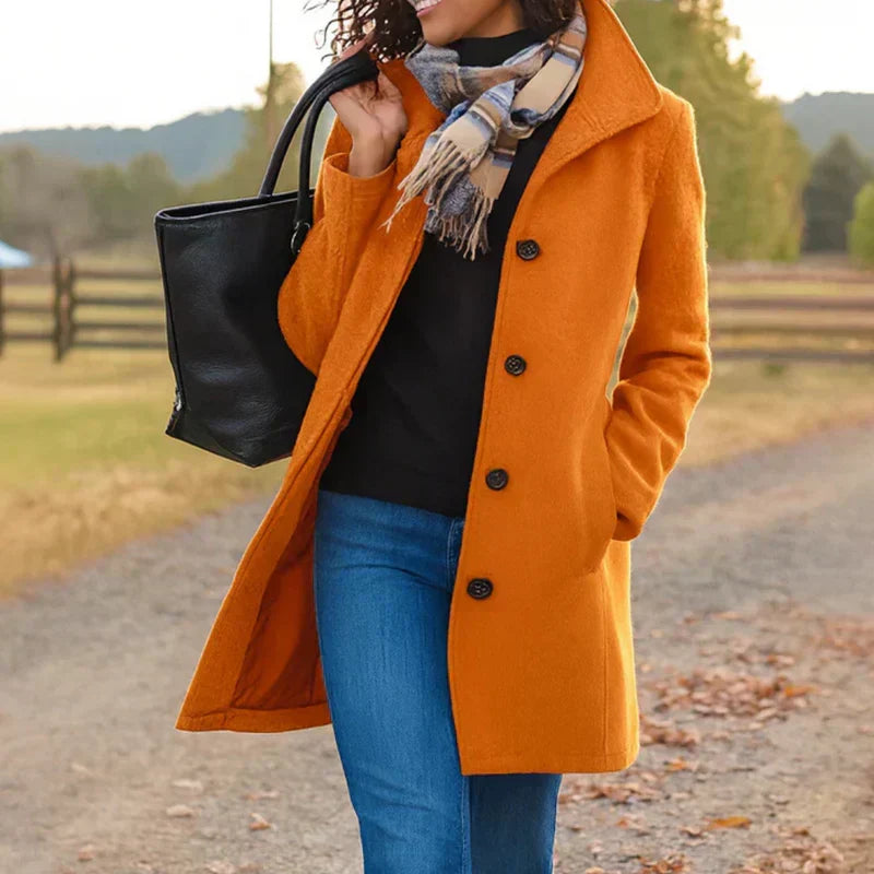 A woman wearing an elegant camel button-through coat over a sweater on a crisp fall day.