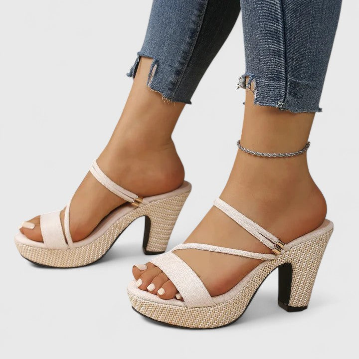 A woman in black strappy platform sandals with a chunky block heel, poised at an evening event.