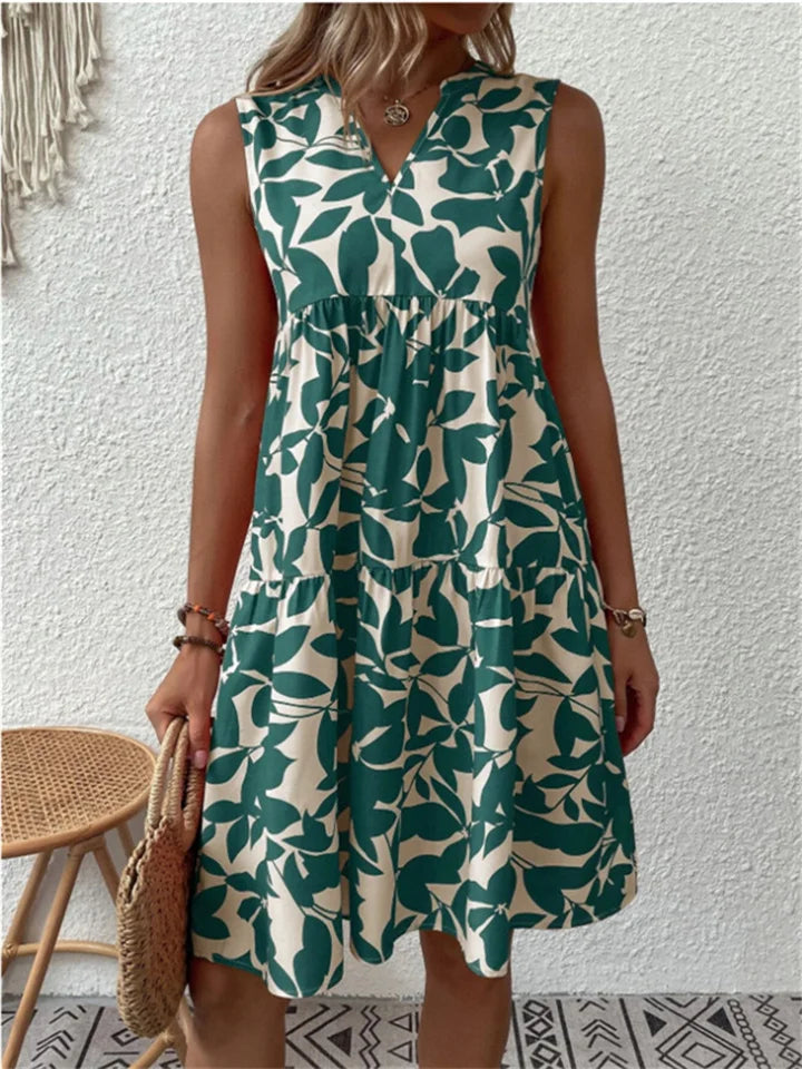 Woman wearing the Deborah sleeveless leaf-print midi dress in green, relaxing outdoors on a warm afternoon.