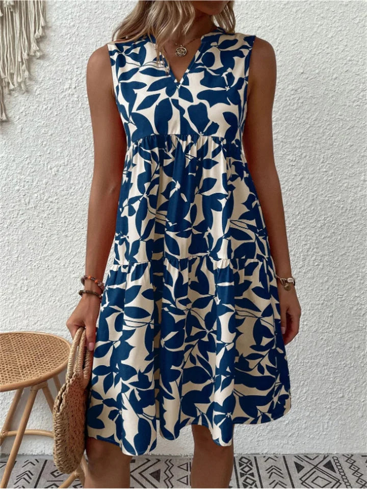 Woman wearing the Deborah sleeveless leaf-print midi dress in green, relaxing outdoors on a warm afternoon.