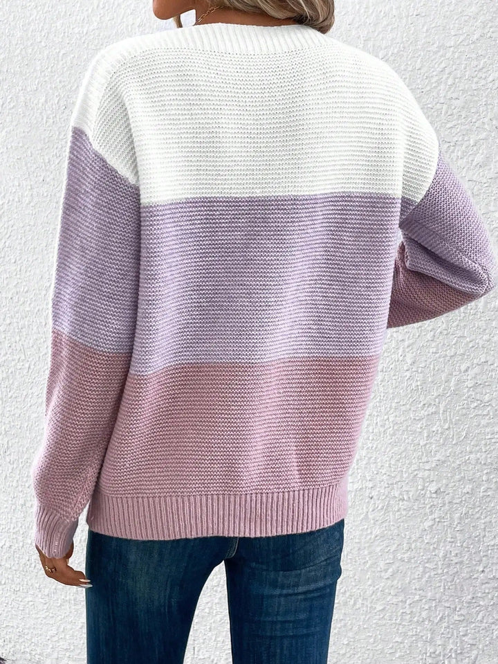A woman wearing a soft colour block sweater in cream, taupe and beige with a wide boat neckline.
