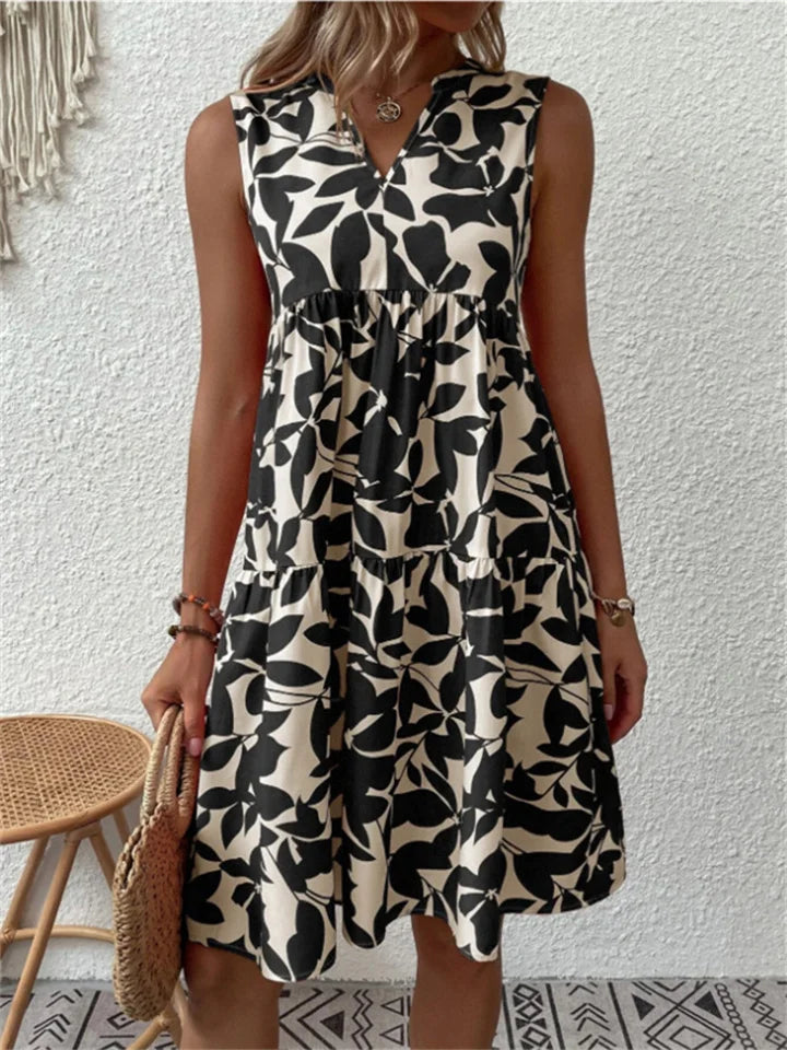 Woman wearing the Deborah sleeveless leaf-print midi dress in green, relaxing outdoors on a warm afternoon.