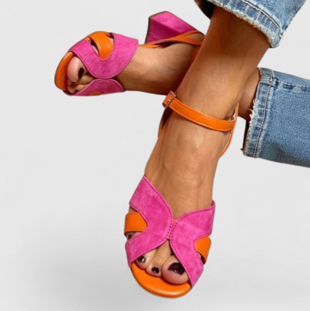 A woman wearing pink and orange open-toe block-heel sandals with an ankle strap, standing comfortably in a summer outfit.