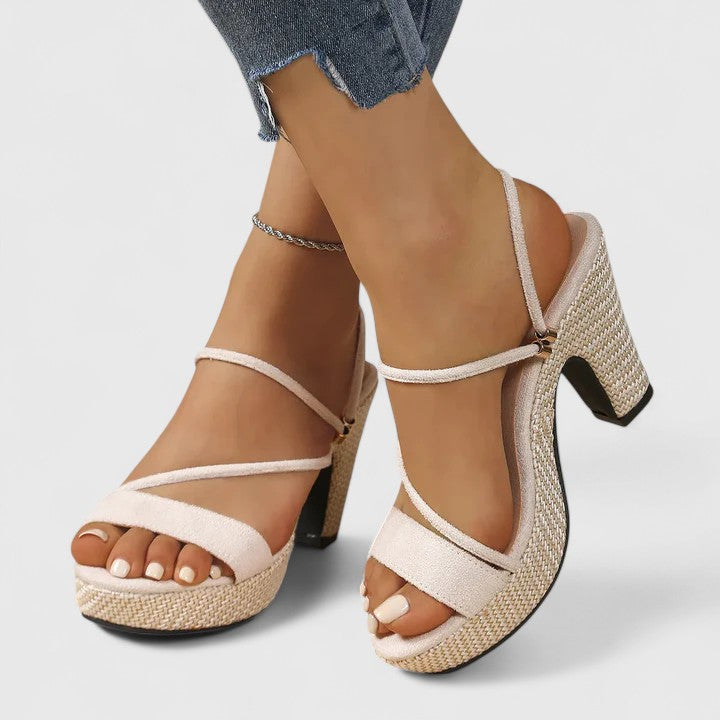 A woman in black strappy platform sandals with a chunky block heel, poised at an evening event.