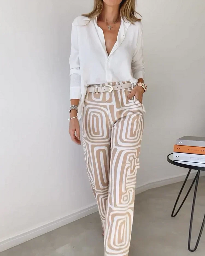A woman wearing a plain button-up top with geometric-print pants and a belt at the waist.