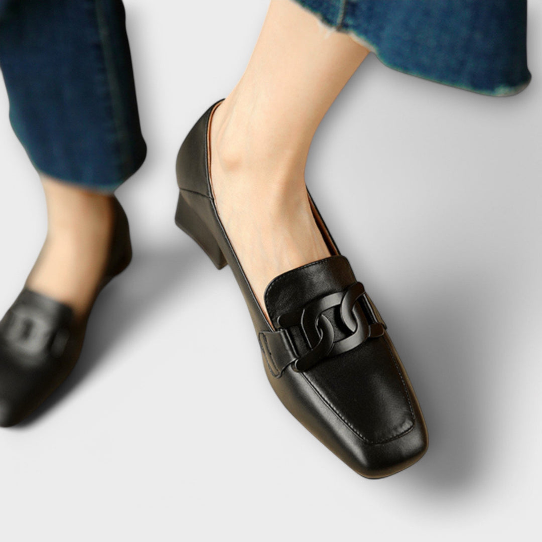 A pair of soft beige square-toe loafers with a chain-link ornament across the front.