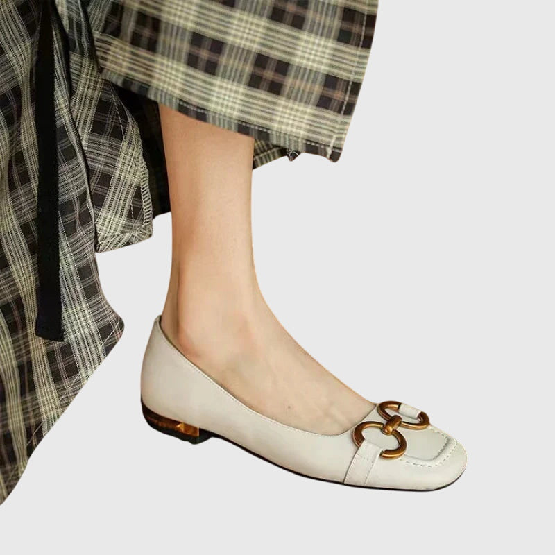 A pair of black slip-on flats with a polished gold ring detail across the toe.