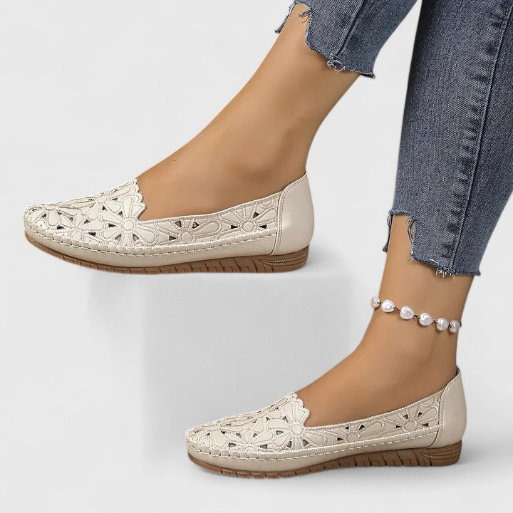 A woman wearing white floral cut-out slip-on flats on a warm, sunny day.