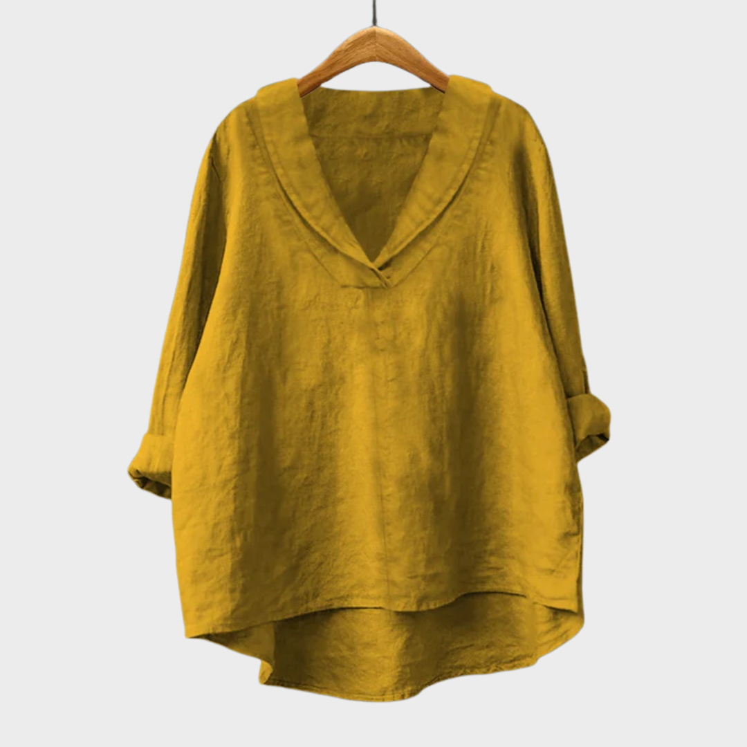 A woman wearing an elegant plain summer blouse with a flowing drape, styled with pants.