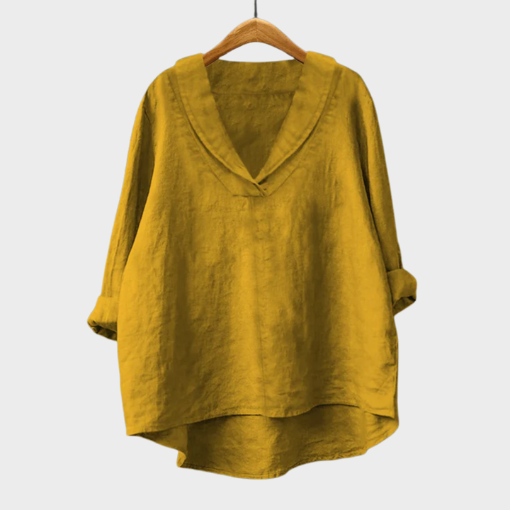 A woman wearing an elegant plain summer blouse with a flowing drape, styled with pants.