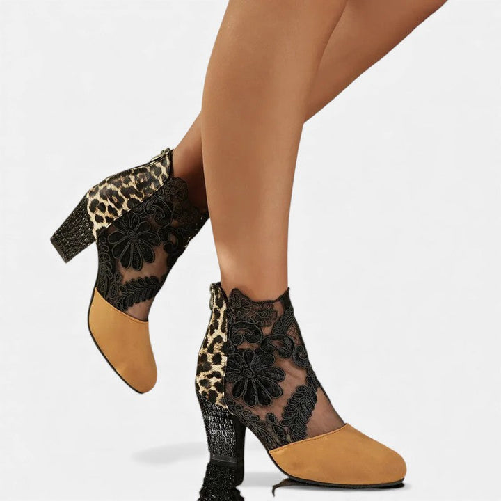 A woman wearing wine block-heel shoes with a sheer black floral-lace ankle overlay and a crystal-set heel