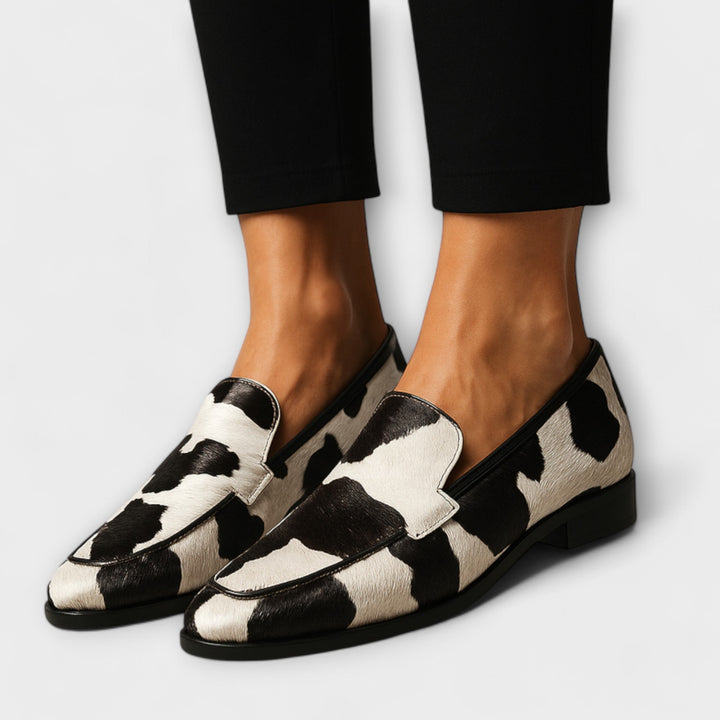 A woman wearing black-and-white cow-print loafers with a simple, modern outfit