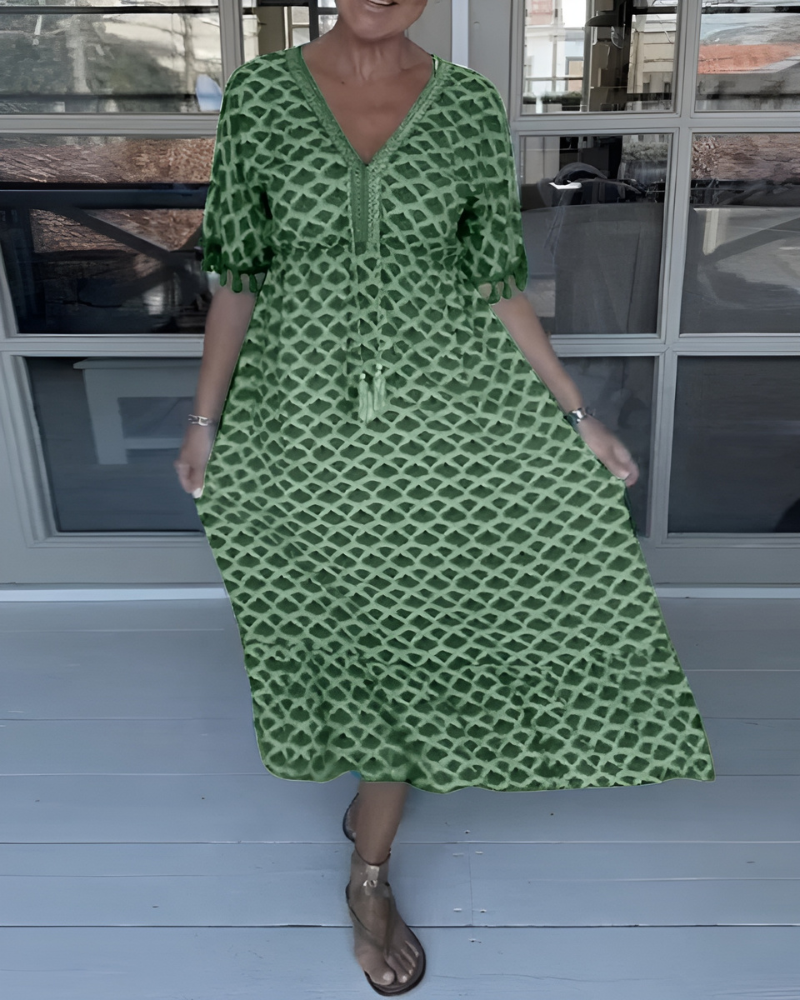 A woman walking near the coast in a flowing blue diamond-lattice print maxi dress with a tassel-trimmed neckline.