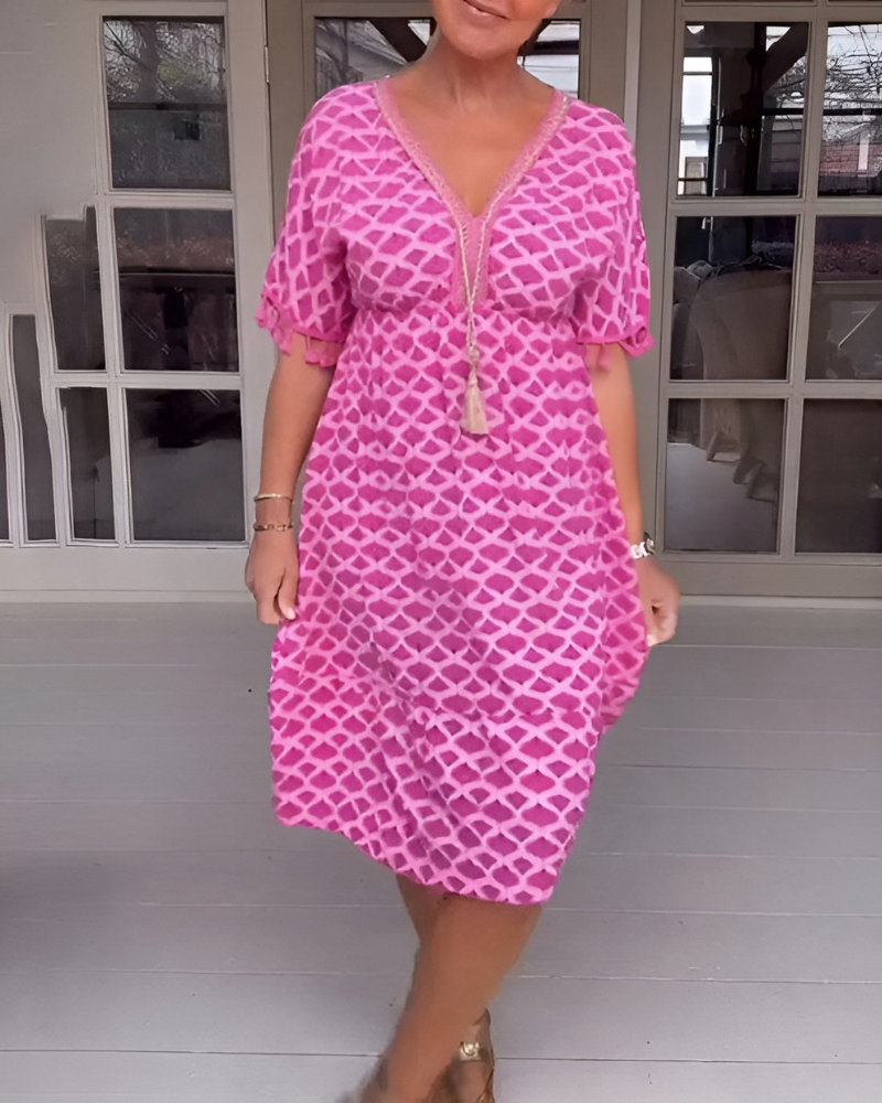 A woman walking near the coast in a flowing blue diamond-lattice print maxi dress with a tassel-trimmed neckline.