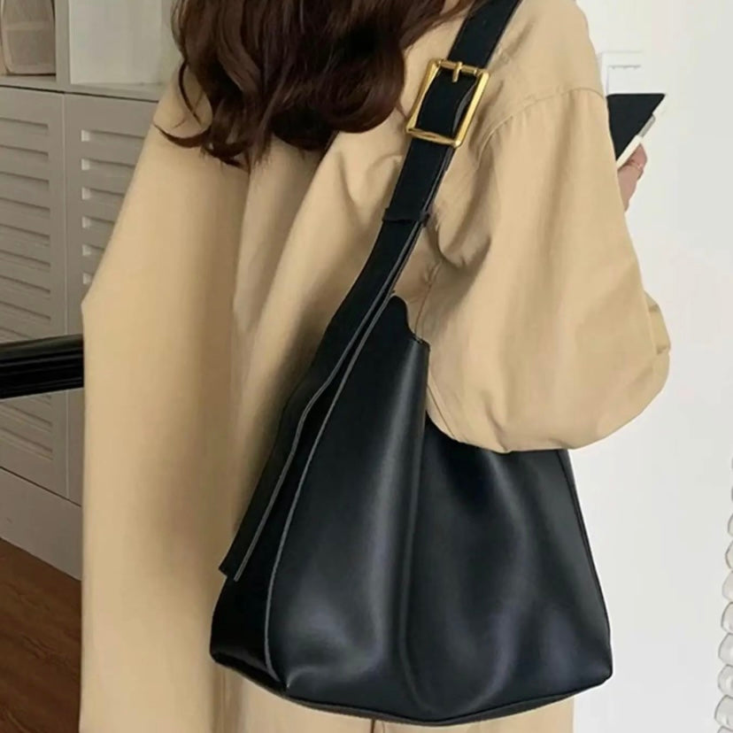 A tan bucket-style shoulder bag with an adjustable buckled strap