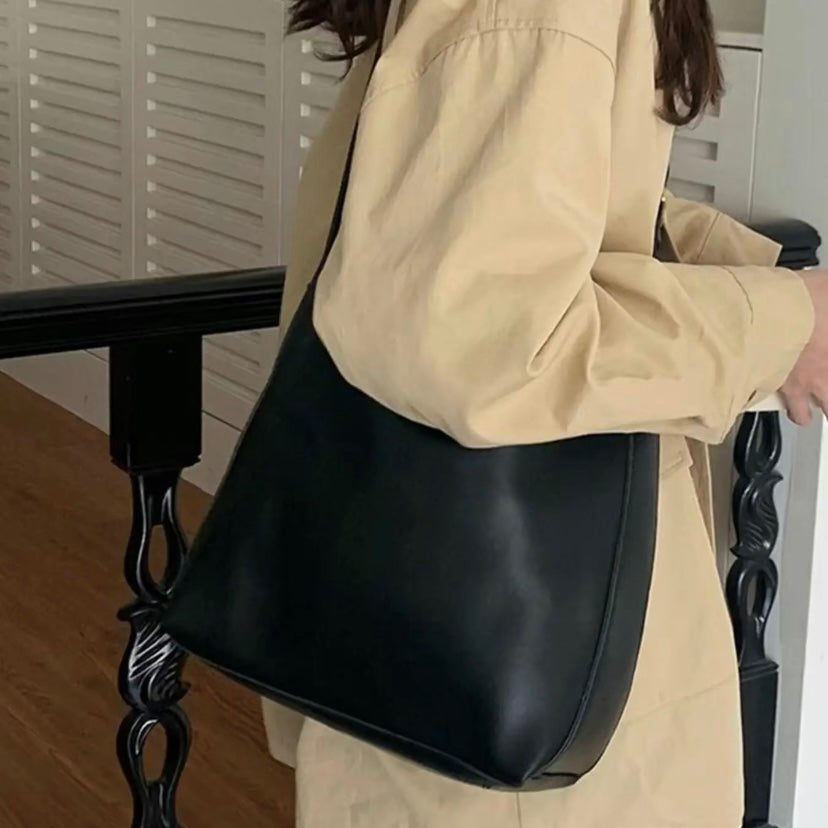 A tan bucket-style shoulder bag with an adjustable buckled strap