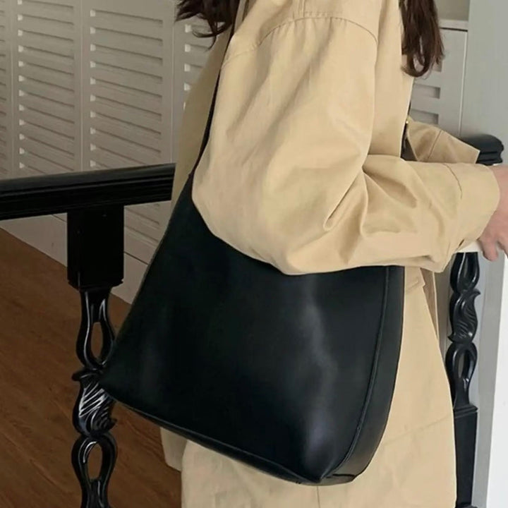 A tan bucket-style shoulder bag with an adjustable buckled strap