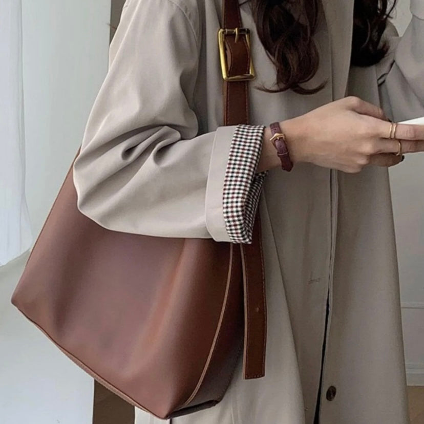 A tan bucket-style shoulder bag with an adjustable buckled strap