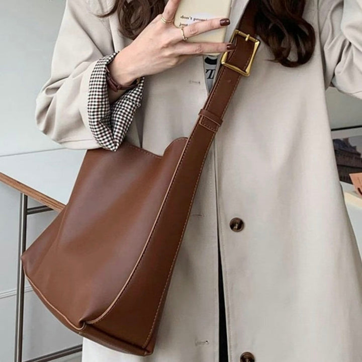 A tan bucket-style shoulder bag with an adjustable buckled strap