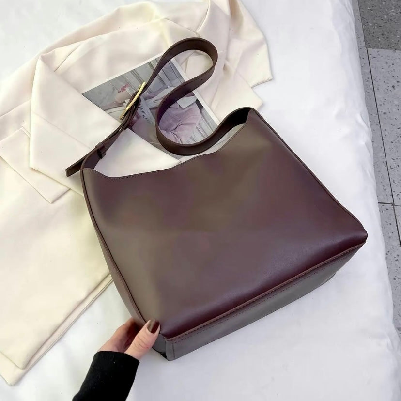 A tan bucket-style shoulder bag with an adjustable buckled strap