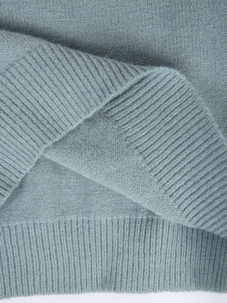 A woman wearing a soft powder-blue sweater with a cream, tan and black Nordic yoke pattern