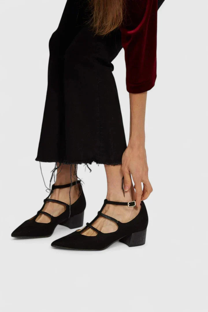 A woman walking through the city in black pointed-toe block heels with slim ankle straps, relaxed and confident.