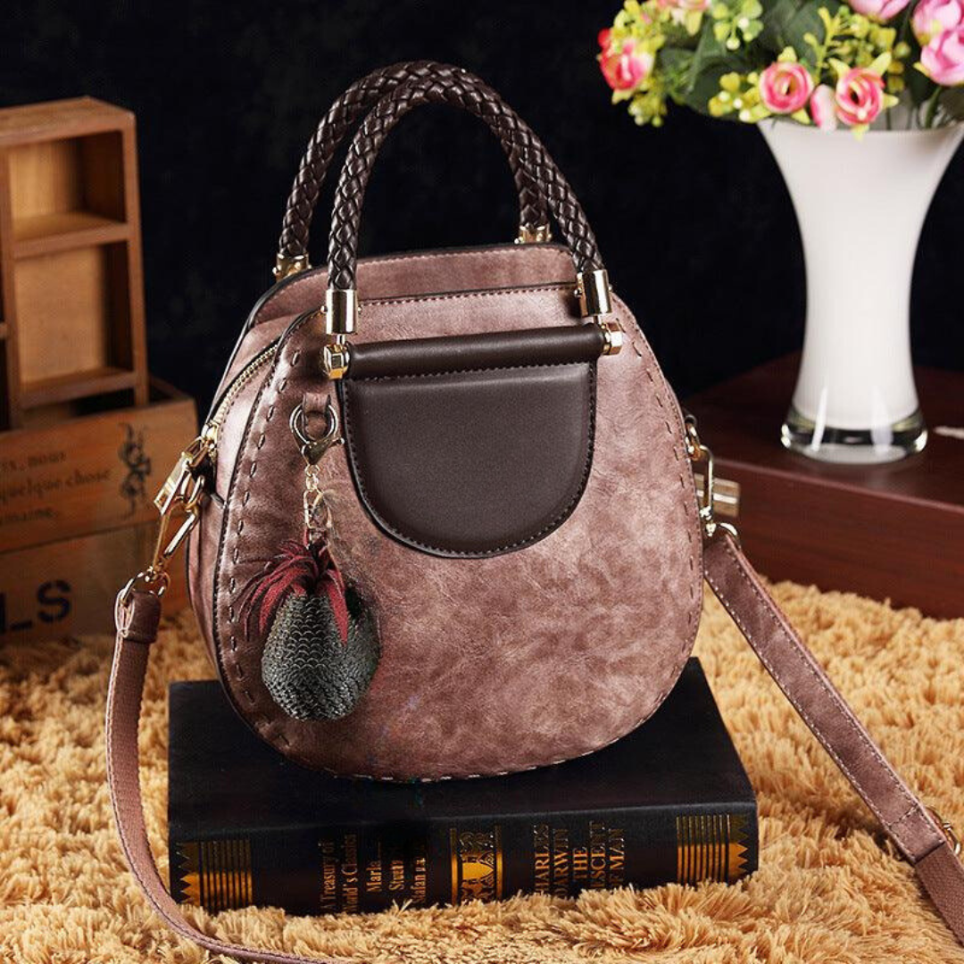 A woman carrying a small round top-handle handbag with a rich finish