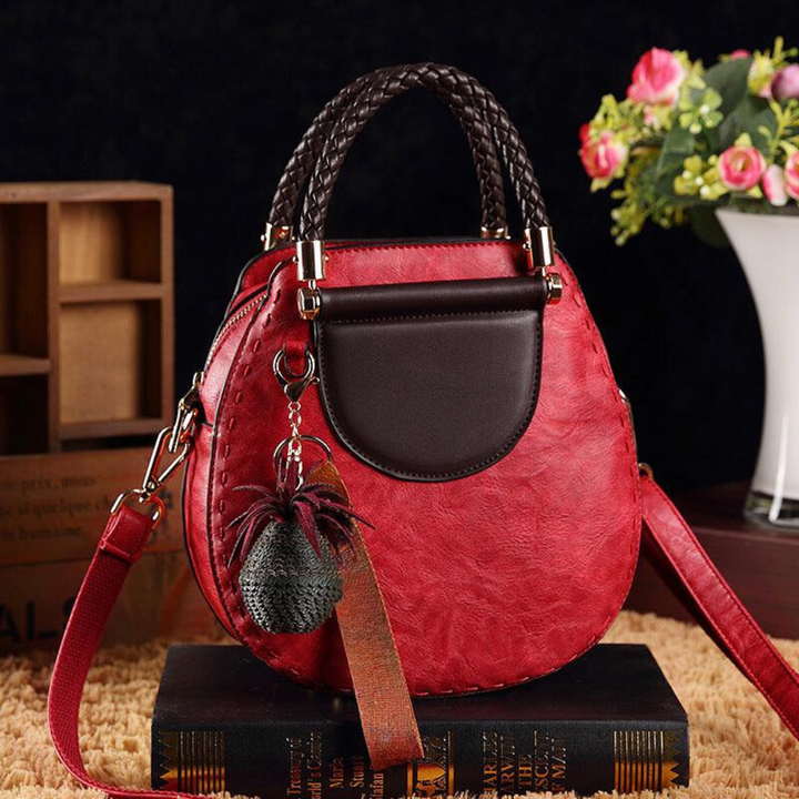 A woman carrying a small round top-handle handbag with a rich finish