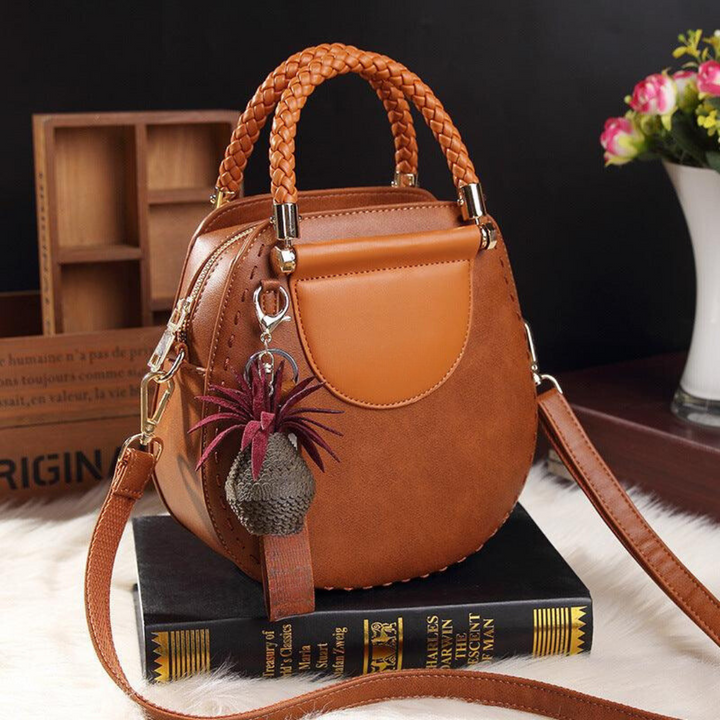 A woman carrying a small round top-handle handbag with a rich finish