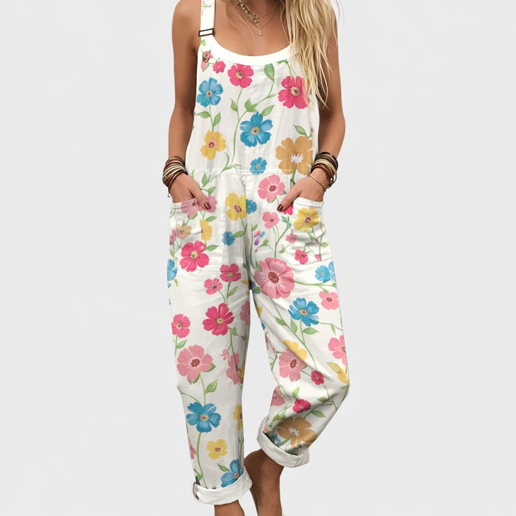 Woman wearing cream overalls scattered with small pink, blue and yellow flowers, adjustable straps, cheerful and relaxed.