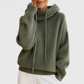 A woman wearing a cosy soft green hoodie with a drawstring hood and white pants.