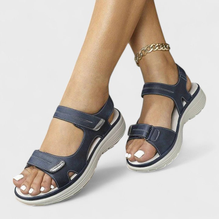 A woman walking gracefully in blue support sandals with a broad, cushioned footbed.
