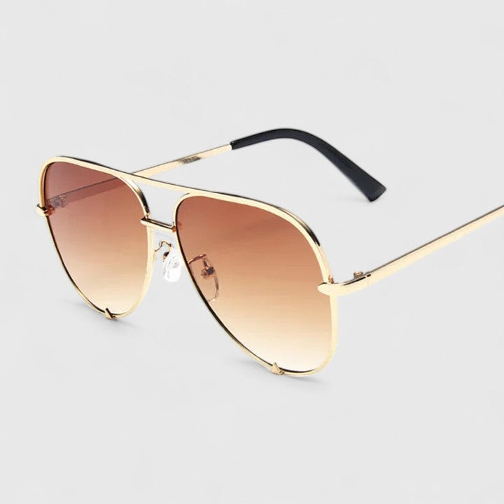 A woman by the sea wearing aviator sunglasses with gradient mirror lenses, relaxed in the sun.