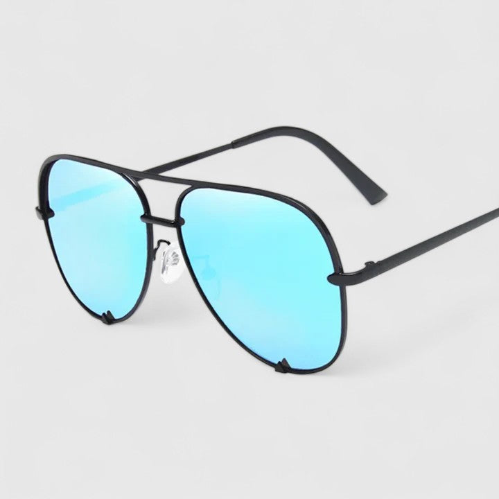 A woman by the sea wearing aviator sunglasses with gradient mirror lenses, relaxed in the sun.