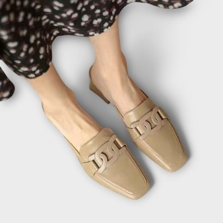 A pair of soft beige square-toe loafers with a chain-link ornament across the front.
