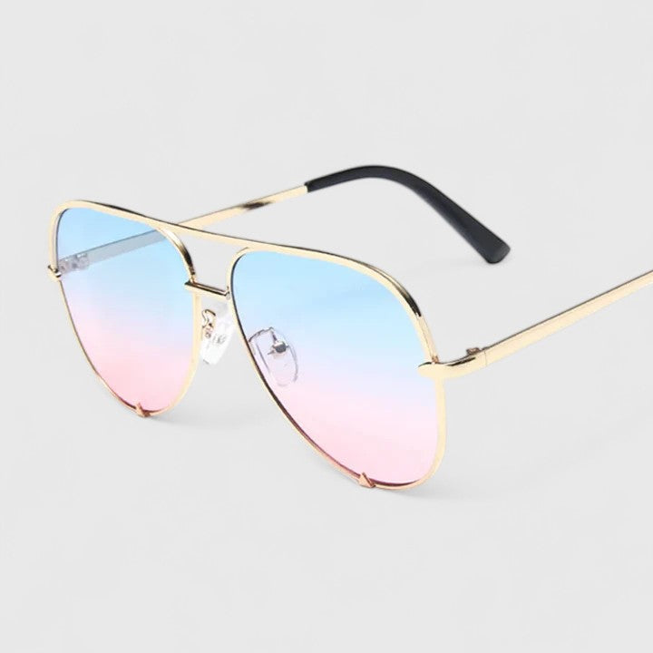 A woman by the sea wearing aviator sunglasses with gradient mirror lenses, relaxed in the sun.
