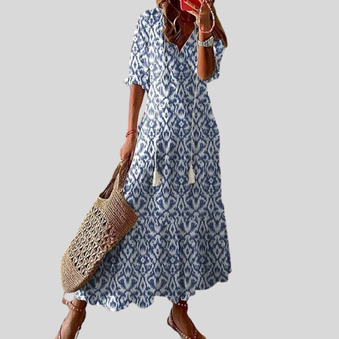 Woman wearing the Jacqueline™ boho maxi dress with fringe details and a V-neckline, relaxed in a warm outdoor setting.
